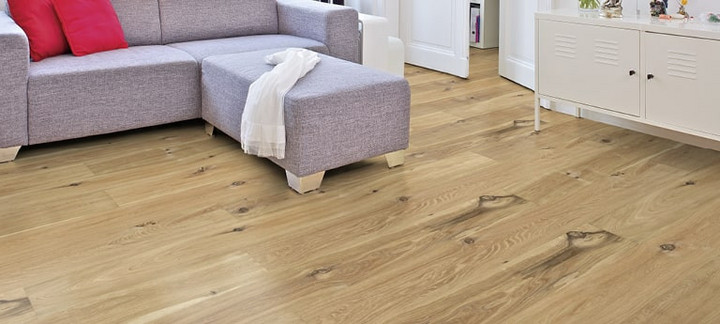 Im Wohnzimmer ist Parkett in Langdielen-Optik verlegt. Dazu passt ein Ecksofa mit bunten Kissen.