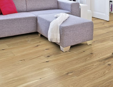 Im Wohnzimmer ist Parkett in Langdielen-Optik verlegt. Dazu passt ein Ecksofa mit bunten Kissen.