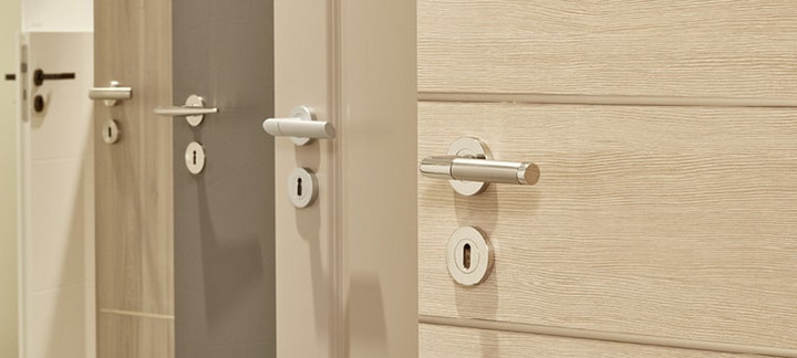 Mehrere nebeneinander angeordnete Türblätter in unterschiedlichen Farbtönen (weiß, holzähnlich, grau) mit integrierten Türgriffen.